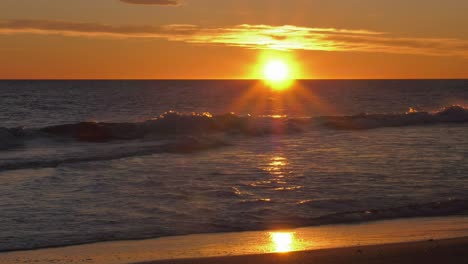 Sun-rising-over-waves-on-beach,-slow-motion-coastal-sunrise,-wide-shot,-mediterranean-sea,-spain