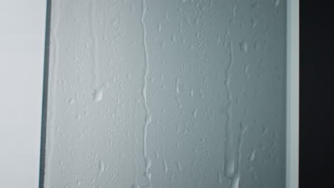 Wassertropfen,-Die-Düster-Wie-Regentropfen-In-Einem-Heißen-Badezimmer-Auf-Dem-Duschglas-Herunterlaufen,-In-Nahaufnahme