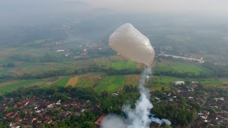 Festive-flying-hot-air-balloon-with-exploding-firecrackers-in-Indonesia,-aerial