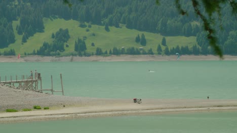 Medium-shot,-Tree-branch-blown-by-the-wind-in-Italy,-People-taking-pictures-of-kite-boarding-on-Reschensee-on-a-bright-sunny-day