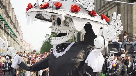 A-giant-skeleton-puppet-operated-by-puppeteers-in-costumes-passes-by-at-the-Day-of-the-Dead-Parade-in-Mexico-City,-Mexico