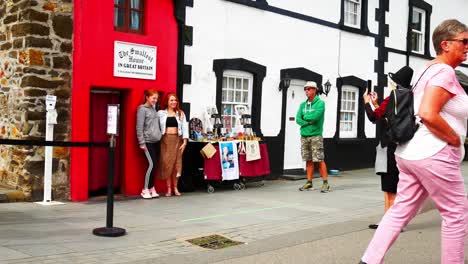 Traditional-Welsh-tourist-guide-photographing-tourists-outside-famous-red-tiny-house-Wales-attraction-Conwy
