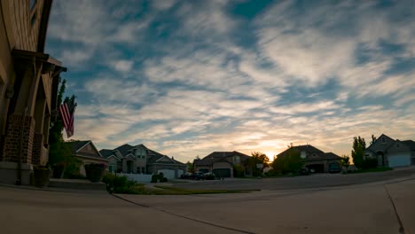 Sunset-cloudscape-over-a-suburban-neighborhood-with-a-US-flag-posted-on-one-house---static-time-lapse