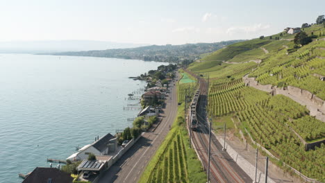 Aerial-of-train-driving-through-beautiful-Swiss-landscape-with-hills-and-a-large-lake