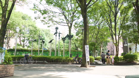 People-walk-in-a-peaceful-Tokyo-park-on-a-sunny-day-with-statues-in-the-background-in-Japan