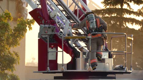 Firefighter-In-Safety-Helmet-And-Uniform-With-Fire-Extinguisher-On-His-Back-Climbs-On-The-Ladder-Of-A-Firetruck