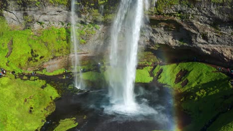 Powerful-Stream-of-water-falling-down-from-Seljalandsfoss-Waterfall-With-Tourist-Strolling-At-Summer-In-Iceland---Aerial
