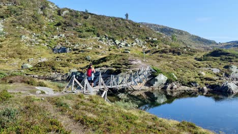 Mochilero-Turístico-Disfrutando-De-La-Libertad-Y-El-Silencio-En-La-Naturaleza-Noruega---Cruzando-Un-Puente-De-Madera-En-El-Paisaje-Montañoso-De-Hamlagro-Voss