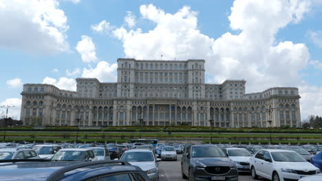 Aparcamiento-Y-Tráfico-Diurno-En-La-Carretera-De-La-Ciudad-De-Bucarest,-Rumania-Con-El-Edificio-Del-Palacio-Del-Parlamento-En-Segundo-Plano
