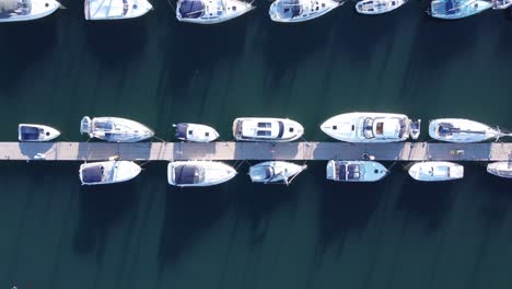 A-top-down-drone-shot-of-a-pontoon,-flying-to-the-right,-with-many-yachts-and-motorboats-moored-up