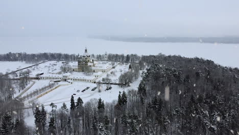Frozen-white-Kaunas-lagoon-and-Pazaislis-monastery-covered-in-snow-during-heavy-snowfall,-aerial-drone-view