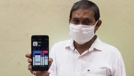 Portrait-of-an-Indian-man-wearing-face-mask-showing-mobile-phone-with-Umang-app-towards-the-camera