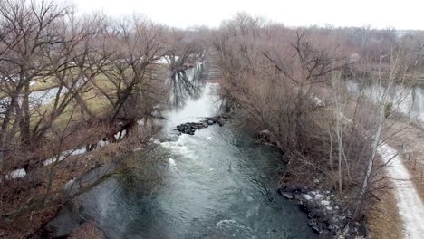 Small-river-dam-and-rapids-on-scenic,-idyllic,-willow-tree-lined-flowing-river-in-winter-in-rural-countryside-in-Boise,-Idaho,-USA