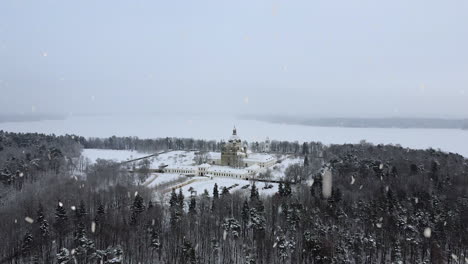Pazailis-monastery-in-Lithuania-covered-in-snow-during-snowfall,-aerial-ascend-view