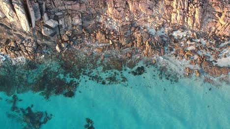 Aerial-drone-topdown-moving-away-from-the-ocean-with-crystal-clear-calm-turquoise-water-in-cape-naturaliste,-Western-Australia