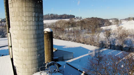 AERIAL-Descending-Over-Snow-Covered-Farmland-With-Silos,-Snowing