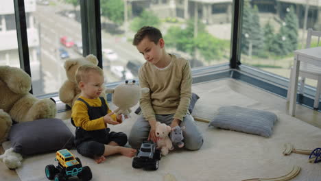 Two-brothers-playing-with-soft-toys.-Adorable-children-sitting-on-rug-at-home.