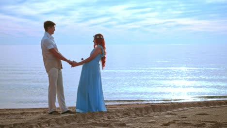 Couple-holding-hands-on-sea-beach-at-sunrise.-Pregnant-couple-beach
