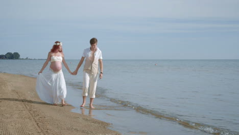 Couple-walking-beach.-Pregnant-couple-on-sea-beach.-Pregnant-woman-on-beach