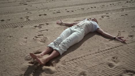 Man-relaxing-on-sand.-Man-making-angel-on-sand.-Man-lying-on-sand