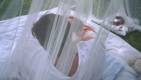Man-and-red-hair-woman-laying-on-white-veil-behind-transparent-cloth-at-park