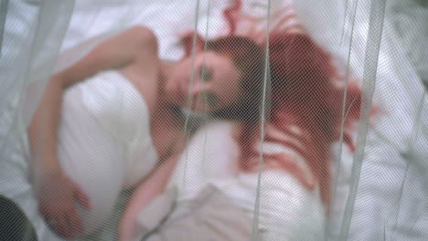 Redhead-woman-lying-on-white-fabric-behind-transparent-veil