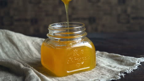 Honey-jar-with-dripper.-Honey-bowl-on-table.-Honey-dripping-in-bottle
