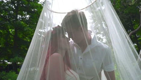 Love-couple-kissing.-Pregnant-couple-kissing-behind-wedding-veil-at-park