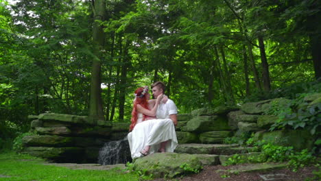 Cheerful-couple-resting-on-stone-near-waterfall-in-forest.-Love-couple-kissing