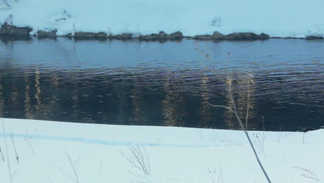 Winter-river.-River-surface-with-light-reflections.-Snow-covered-riverbank