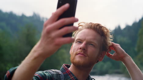 Man-fixing-hairstyle-before-selfie.-Guy-taking-selfie-on-smartphone-in-mountains