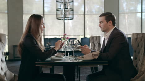 Business-people-using-mobile-phone-at-restaurant.-Business-couple-working-phones