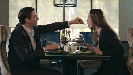 Romantic-couple-eating-at-restaurant.-Man-give-food-to-woman-at-romantic-dinner