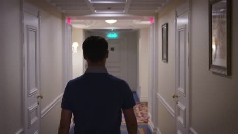 Young-man-in-blue-shirt-walking-along-corridor-at-hallway-hotel-back-view