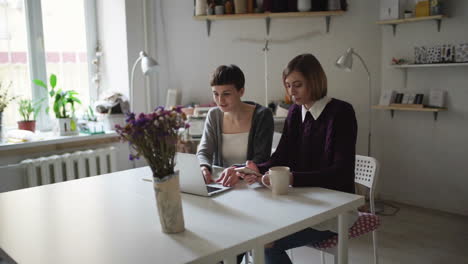 Two-woman-students-at-table-using-notebook-for-online-learning-in-home