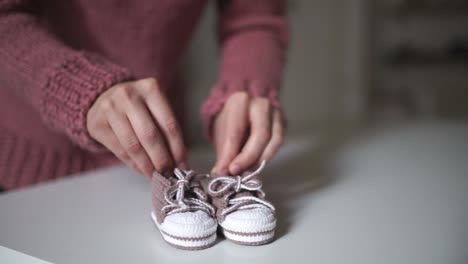 Mother-hands-playing-with-pink-baby-booties.-Knitting-clothes-for-baby