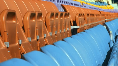 Seating-rows-in-stadium-with-folded-chairs.-Close-up-empty-orange-and-blue-seats