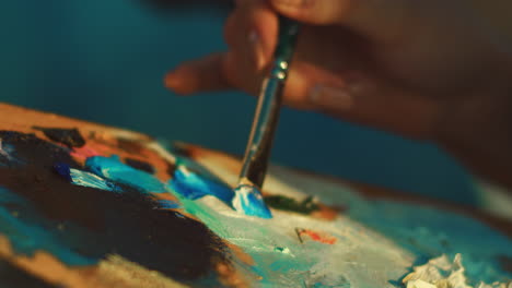 Female-artist-mixing-paints-on-palette-with-brush.-Woman-hand-holding-paintbrush