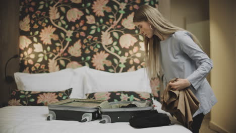 Woman with suitcase sitting on bed in hotel. Young Girl packing