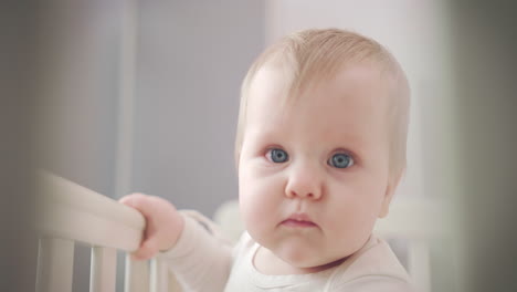 Cute-baby-face-with-blue-eyes.-Infant-baby-standing-in-bed-and-looking-around