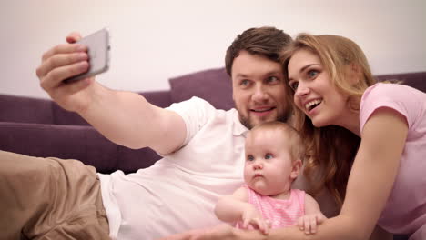 Parents-kissing-baby.-Happy-family-taking-selfie-photo-at-home