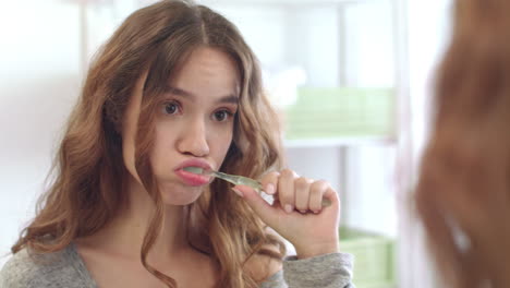 Young-woman-brushing-teeth-in-mirror-at-home-bathroom.-Girl-cleaning-teeth