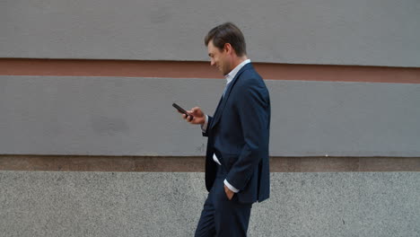 Side-view-businessman-walking-with-phone.-Man-looking-into-smartphone-outdoors