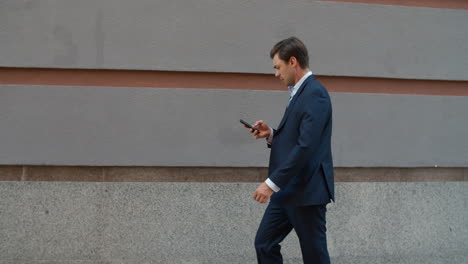 Side-view-business-man-walking-with-phone.-Man-using-phone-near-modern-building