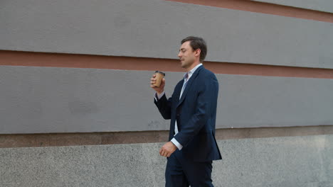 Smiling-man-drinking-coffee-at-street.-Businessman-walking-to-work-with-coffee