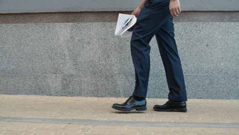 Cropped-image-man-walking-with-documents.-Closeup-man-wearing-shoes-outdoor