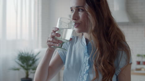 Beautiful-woman-talking-via-headphones-in-white-kitchen.-Girl-drinking-water.