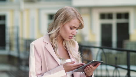 Closeup-woman-working-on-touchpad-at-street.-Woman-using-tablet-in-pink-suit
