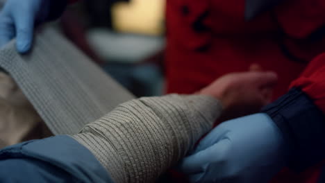 Closeup-ambulance-paramedic-in-gloves-wrapping-patient-hand-with-elastic-bandage