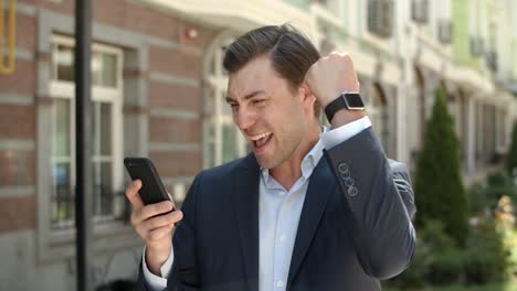 Closeup-business-man-receiving-good-news-at-street.-Man-using-smartphone-outdoor